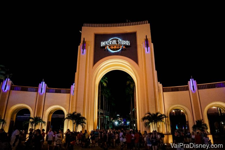 Foto do portal da Universal Studios iluminado durante à noite, com muitos visitantes circulando 