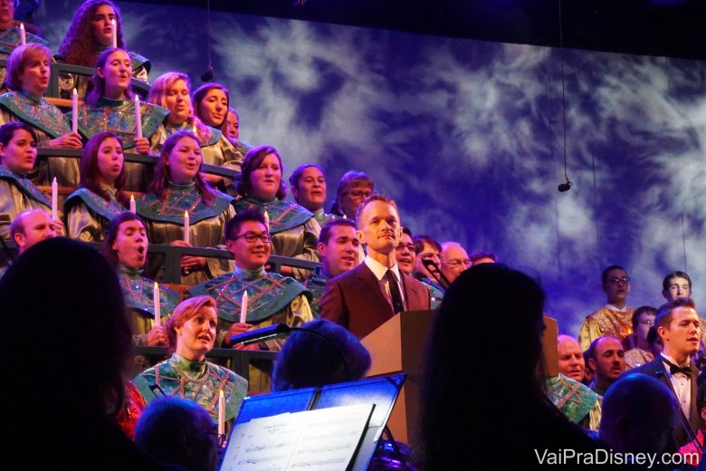 Foto do coral Candlelight Processional no Epcot, com o ator Neil Patrick Harris à frente como narrador. 