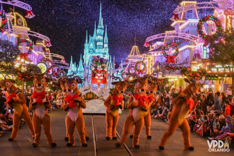 Foto da parada de Natal da Disney, com as renas do Papai Noel na frente e o Papai Noel em um carro atrás. o castelo da Cinderela está ao fundo.