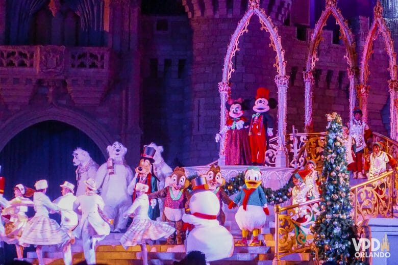 Foto do show de Natal no palco do castelo. O Mickey e a Minnie estão no topo, e vários personagens estão dançando embaixo.