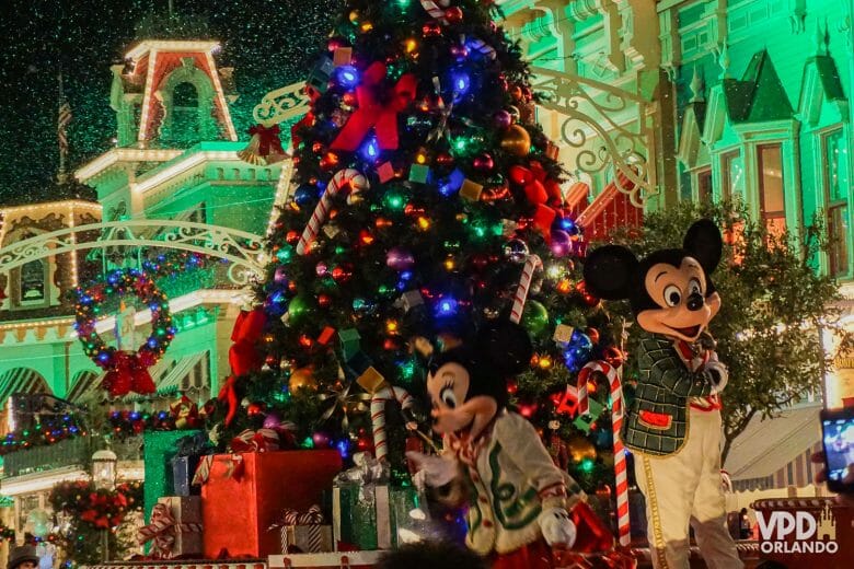 Foto do carro da parada que traz o Mickey e a Minnie, com uma árvore de Natal ao fundo.