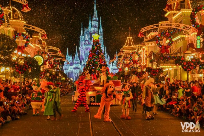 Foto da parada de Natal do Magic Kingdom, com vários personagens dançando, pessoas assistindo ao redor e o castelo ao fundo. 