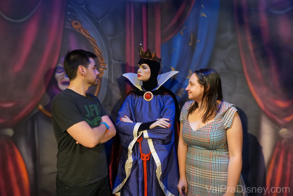 Foto da Renata e do Felipe com a Rainha Má da Branca de Neve no Storybook Dining. O Felipe está de braços cruzados encarando a Rainha e ela está encarando de volta. 