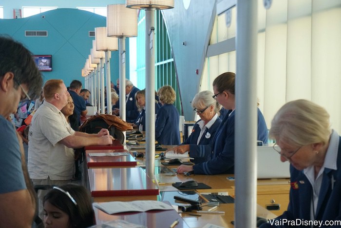 A fila do check-in pode ser grande mas em geral ela anda rápido porque são muitos funcionários atendendo ao mesmo tempo. Foto do balcão do porto durante o check-in, com visitantes e atendentes realizando o procedimento 