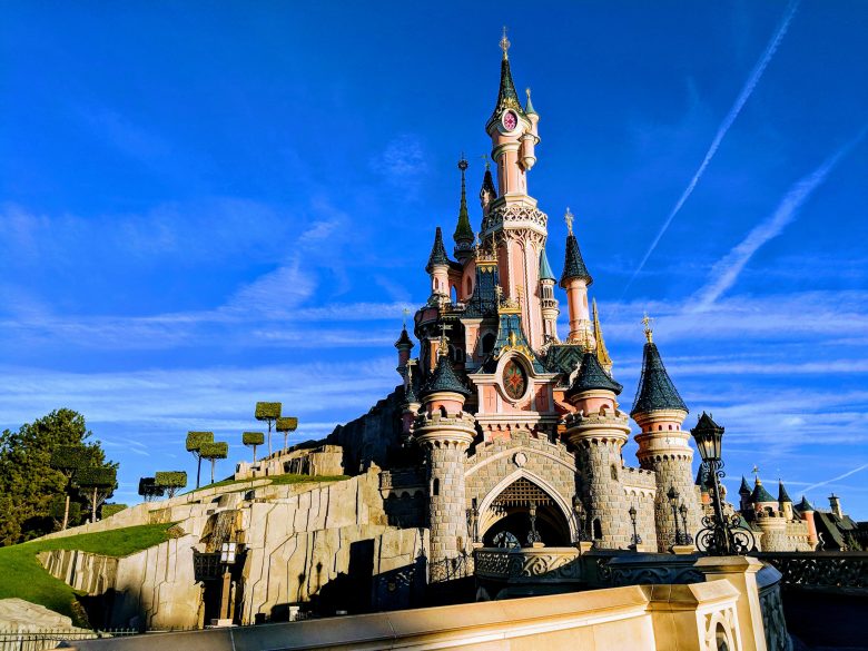 Foto do castelo da Bela Adormecida, na Disneyland de Paris, com o céu azul ao fundo.