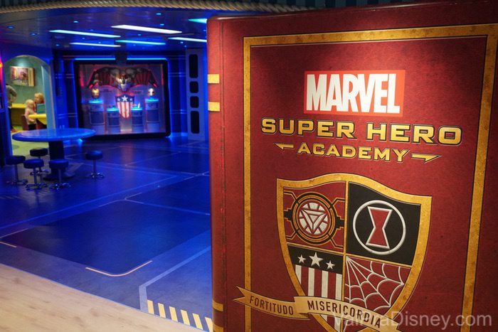 Os clubes infantis valem a visita. São lindos! Foto da entrada do clube infantil da Marvel. A placa diz Marvel Super Hero Academy e tem um brasão com imagens que remetem aos heróis sobre um fundo vermelho 