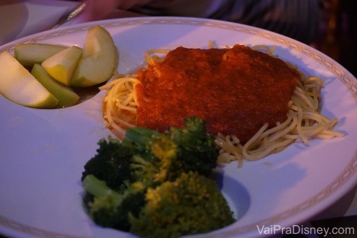 Foto de um prato para crianças no cruzeiro, com macarrão e molho vermelho, brócolis e frutas cortadas 