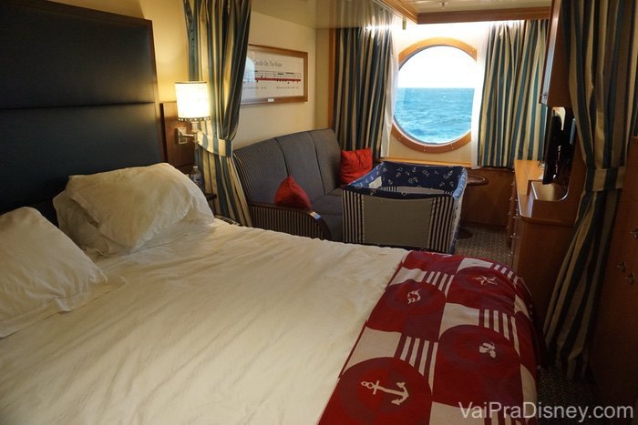 Foto do quarto com janela na cabine do cruzeiro, com o berço montado ao lado da cama 