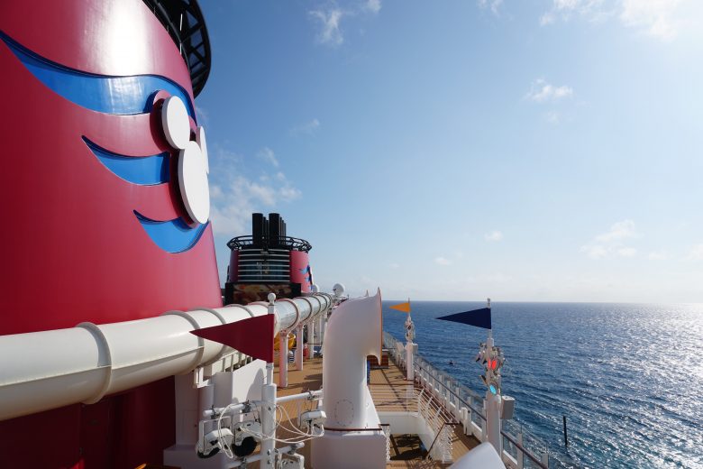 Foto de parte do navio da Disney e do mar. O navio tem detalhes com o Mickey em branco sobre um fundo vermelho e azul. 