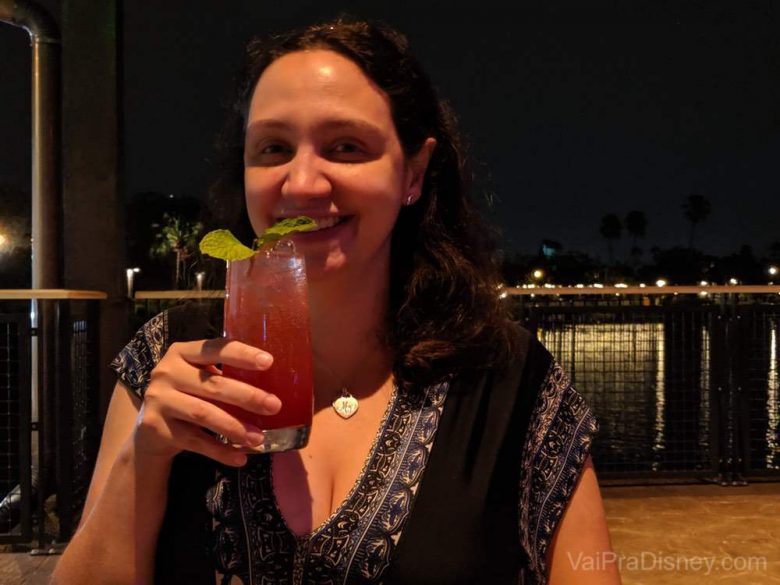 Foto da Renata sorrindo com um drink na mão no Three Bridges Bar & Grill at Villa del Lago, com um lago ao fundo 