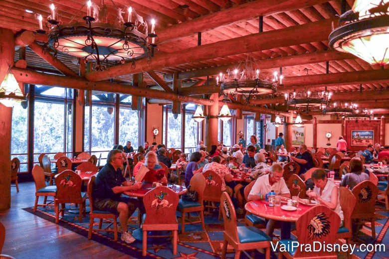 Foto do interior do restaurante, amplo, cheio de mesas com visitantes e decorado todo em madeira 