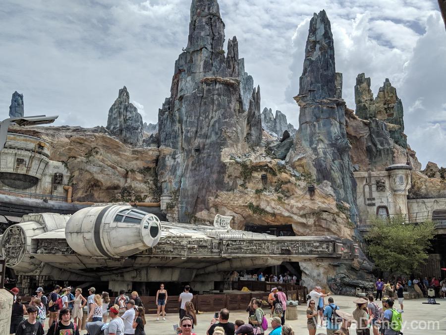 Foto da Star Wars Galaxy's Edge durante o dia, com as montanhas de Batuu ao fundo e a Millenium Falcon mais perto dos visitantes. 