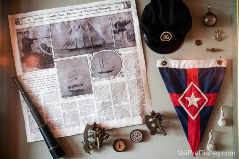 Foto dos pequenos detalhes da decoração dentro do tema náutico de todo o hotel, como uma bandeira, uma luneta e um recorte de jornal. 