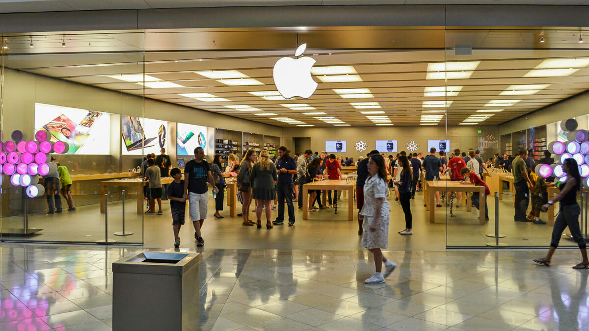 Imagem da fachada da loja da Apple em Orlando. Várias pessoas estão dentro da loja e outras estão passando no corredor.