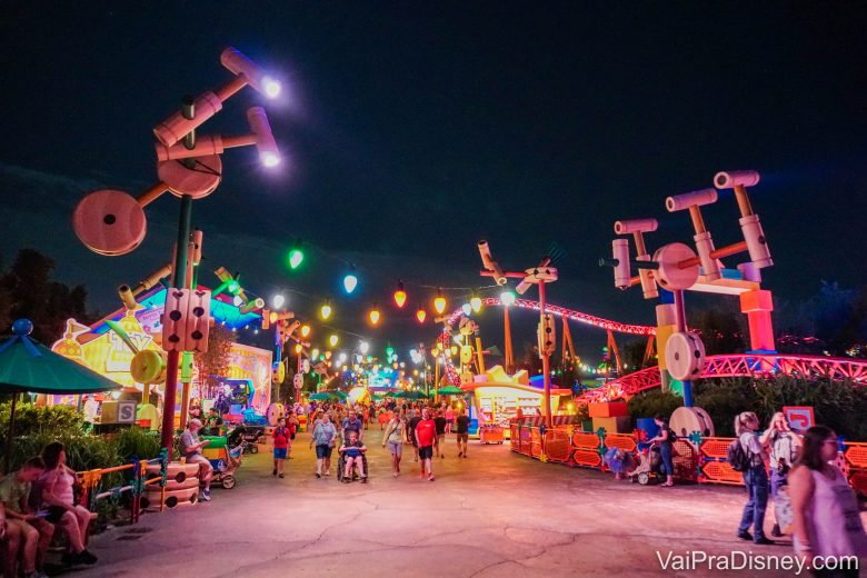 Foto da Toy Story Land, no Hollywood Studios, toda iluminada à noite, com visitantes passeando. 