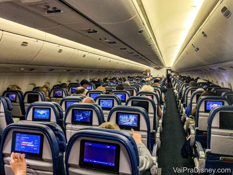 Foto do corredor no interior de um avião. É possível ver a parte de trás de diversas fileiras de poltronas, com as telas acopladas atrás. No avião, vale ter um cuidado redobrado com a higiene em tempos de coronavírus. 