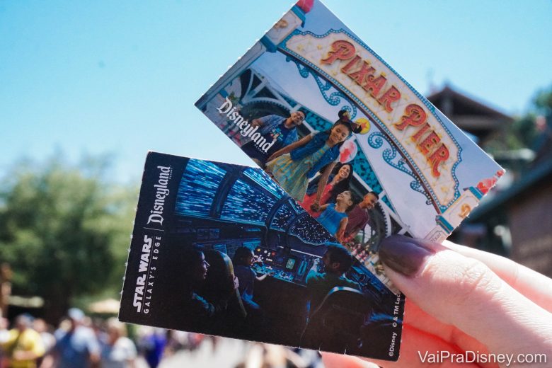 Foto de uma mão segurando os ingressos da Disneyland Califórnia, que são em papel. Eles tem imagens das áreas temáticas dos parques, Star Wars Galaxy's Edge e Pixar Pìer