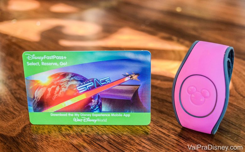 Imagem do cartão magnético que funciona como ingresso da Disney, ao lado de uma MagicBand cor-de-rosa.
