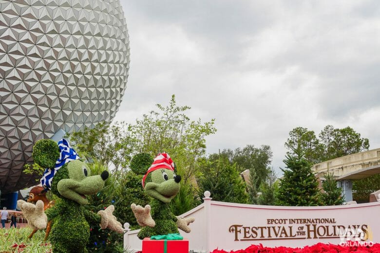 Entrada do Epcot no International Festival of the Holidays. Há topiárias do Mickey e da Minnie usando chapéus de Natal, e a bola do Epcot está do lado esquerdo.