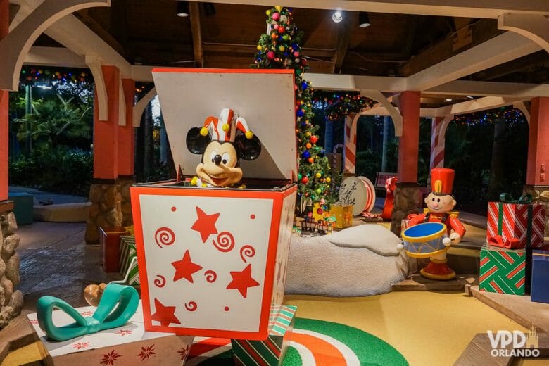 Imagem de um mini golf temático de Natal. Há caixas de presentes espalhados e o Mickey sai de dentro de uma delas.