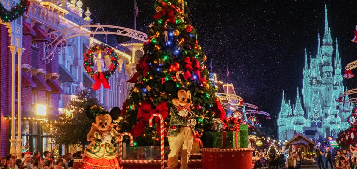 Imagem da parada de Natal do Magic Kingdom. A Minnie e o Mickey estão com roupas temáticas em um carro que possui uma árvore de Natal toda decorada.