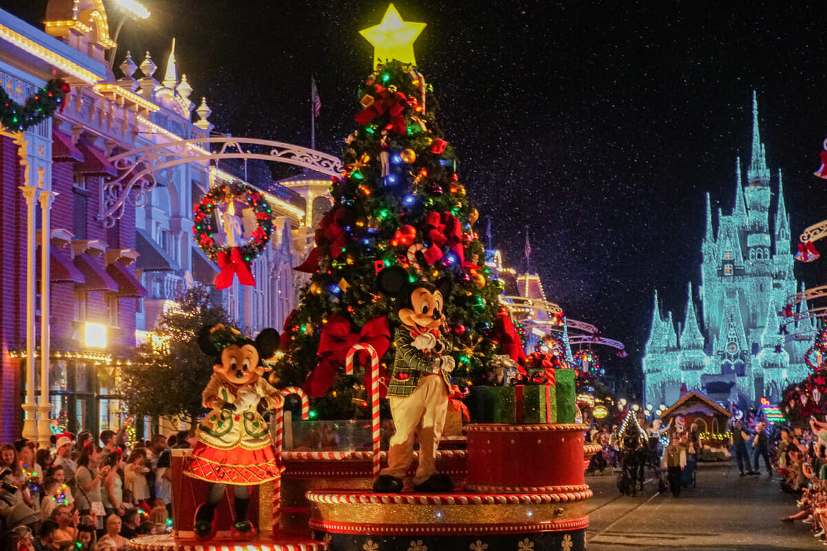 Imagem da parada de Natal do Magic Kingdom. A Minnie e o Mickey estão com roupas temáticas em um carro que possui uma árvore de Natal toda decorada.