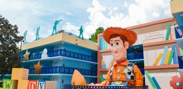 Foto do hotel Disney's All Star Movies, na área do Toy Story. Há uma réplica do Woody gigante rodeado de brinquedos, ao lado do prédio, que é azul.