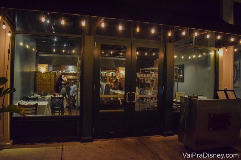 Foto da entrada discreta do Market to Table, com portas de vidro e luzes penduradas 