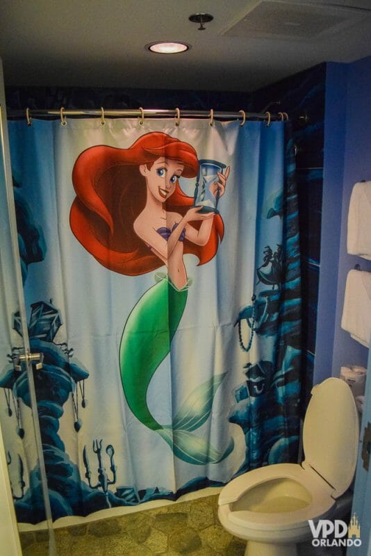 Detalhe da cortina do chuveiro no quarto da Pequena Sereia. A cortina tem a Ariel segurando uma ampulheta. 