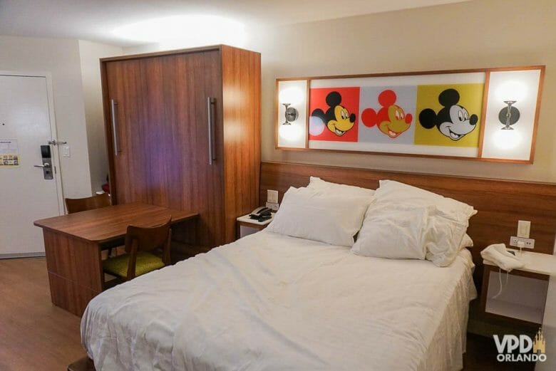 Quarto do hotel Pop Century, com uma cama de casal e outra dobrável que vira uma mesa com duas cadeiras.