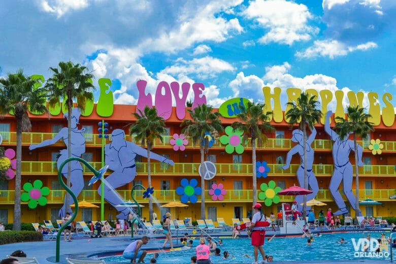 Foto da piscina do hotel Pop Century, que tem decoração dos anos 70, com as palavras "peace", "love" e "happiness" em grandes letras coloridas e pessoas dançando. 