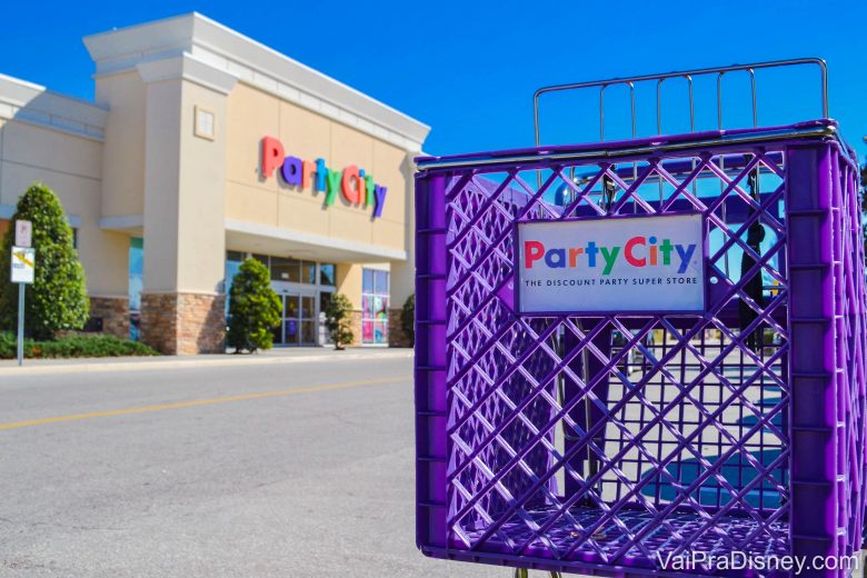 Foto do exterior da loja Party City em Orlando, com seu letreiro multicolorido ao fundo e um carrinho de compras roxo em primeiro plano, com o mesmo letreiro em versão menor 