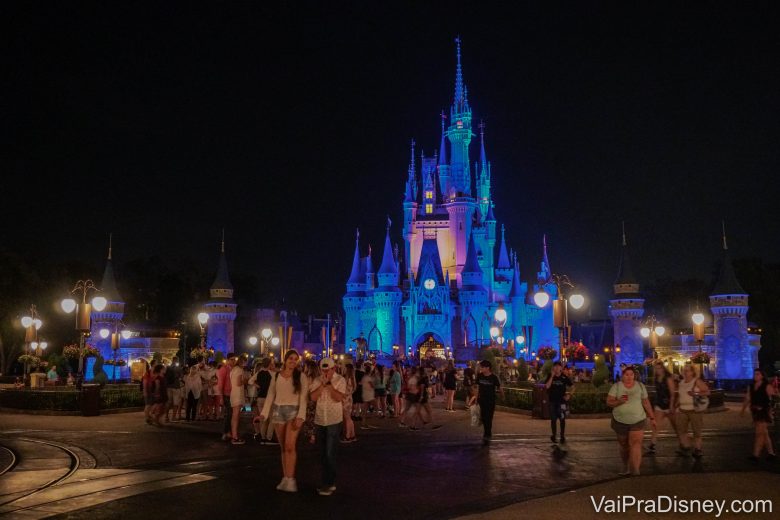 Foto do castelo da Cinderela iluminado em azul à noite e diversos visitantes circulando pelo Magic Kingdom 