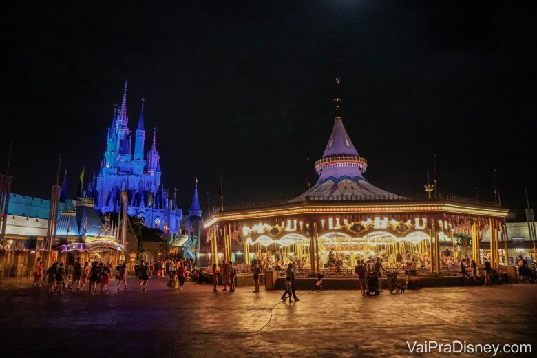 Foto do carrossel da Fantasyland iluminado durante a noite, com o castelo da Cinderela ao fundo