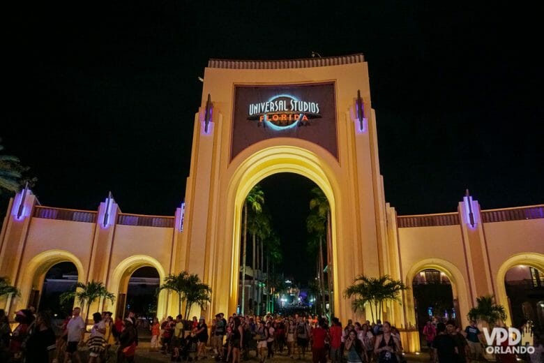 Foto do portal na lateral do Universal Studios, com o título "Universal Studios Florida" iluminado, muitos visitantes transitando e o céu noturno ao fundo