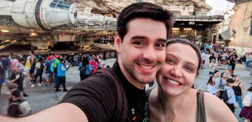 Foto da Renata e do Felipe sorrindo com a Millenium Falcon ao fundo na Star Wars Galaxy's Edge