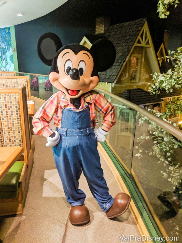 Foto do Mickey fazendeiro que aparece no jantar do Garden Grill, uma das refeições com personagens do complexo Disney. Ele está usando jardineira jeans, camisa xadrez e botas. 