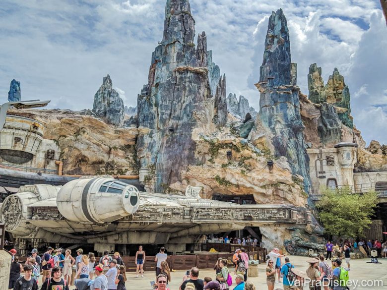 Foto da Star Wars Galaxy's Edge durante o dia, com as montanhas de Batuu ao fundo e a Millenium Falcon mais perto dos visitantes. 