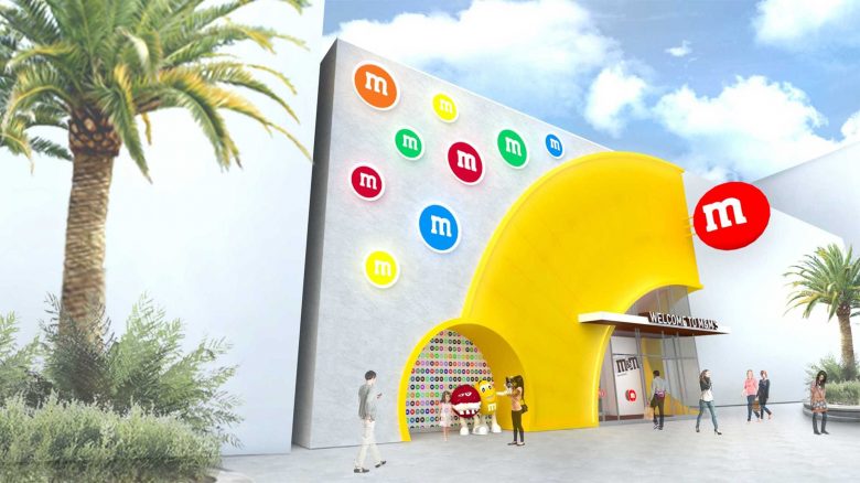 Conceito de como será a fachada da loja da M&M's em Disney Springs, com detalhes em amarelo na porta e M&M's coloridos de decoração 