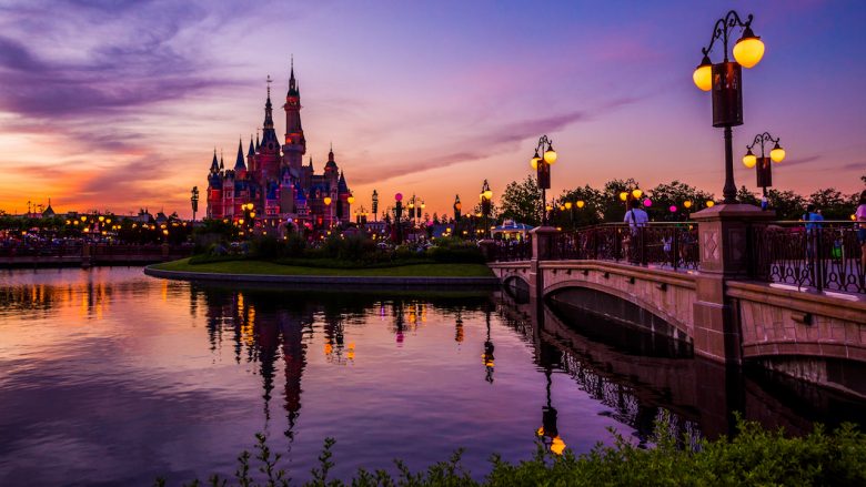 Foto da Disneyland de Shanghai, com o castelo mais ao fundo, no pôr-do-sol, com o céu em tons de roxo, rosa e laranja