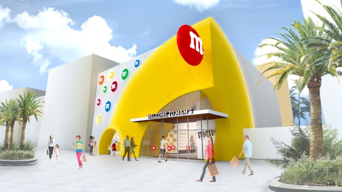 Conceito de como será a fachada da loja da M&M's em Disney Springs, com detalhes em amarelo na porta e M&M's coloridos de decoração 