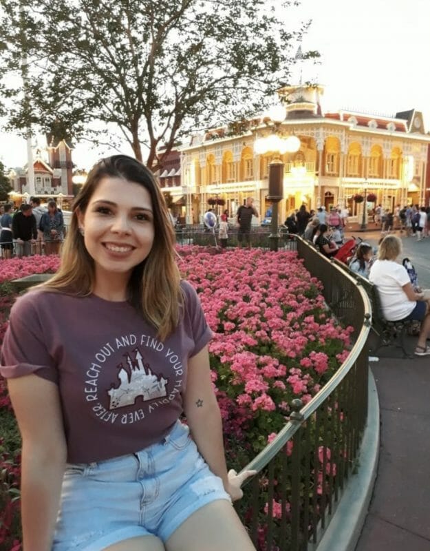 Foto da Helen sentada na grade da Main Street, com flores cor-de-rosa atrás 