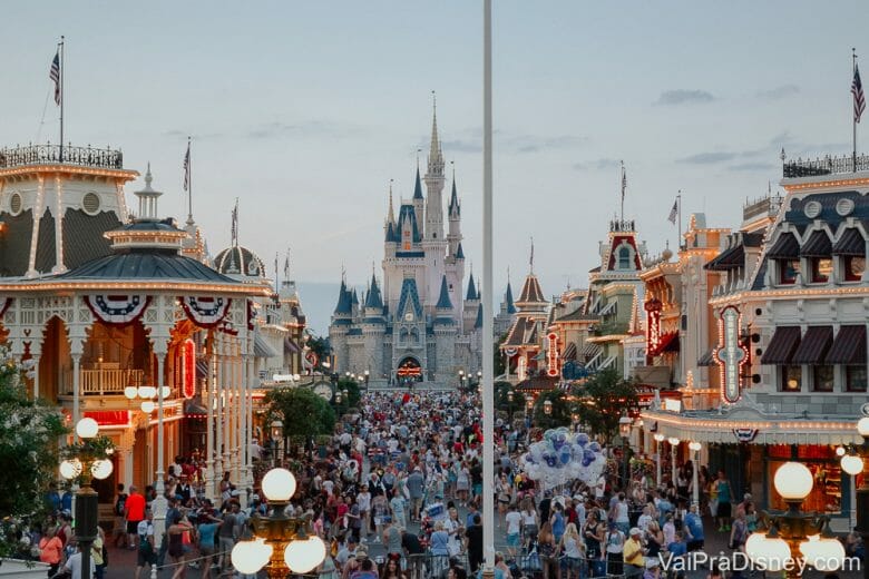 Foto do Magic Kingdom em um dia cheio, com a Main Street começando a ser iluminada e o castelo ao fundo, com o céu claro. 