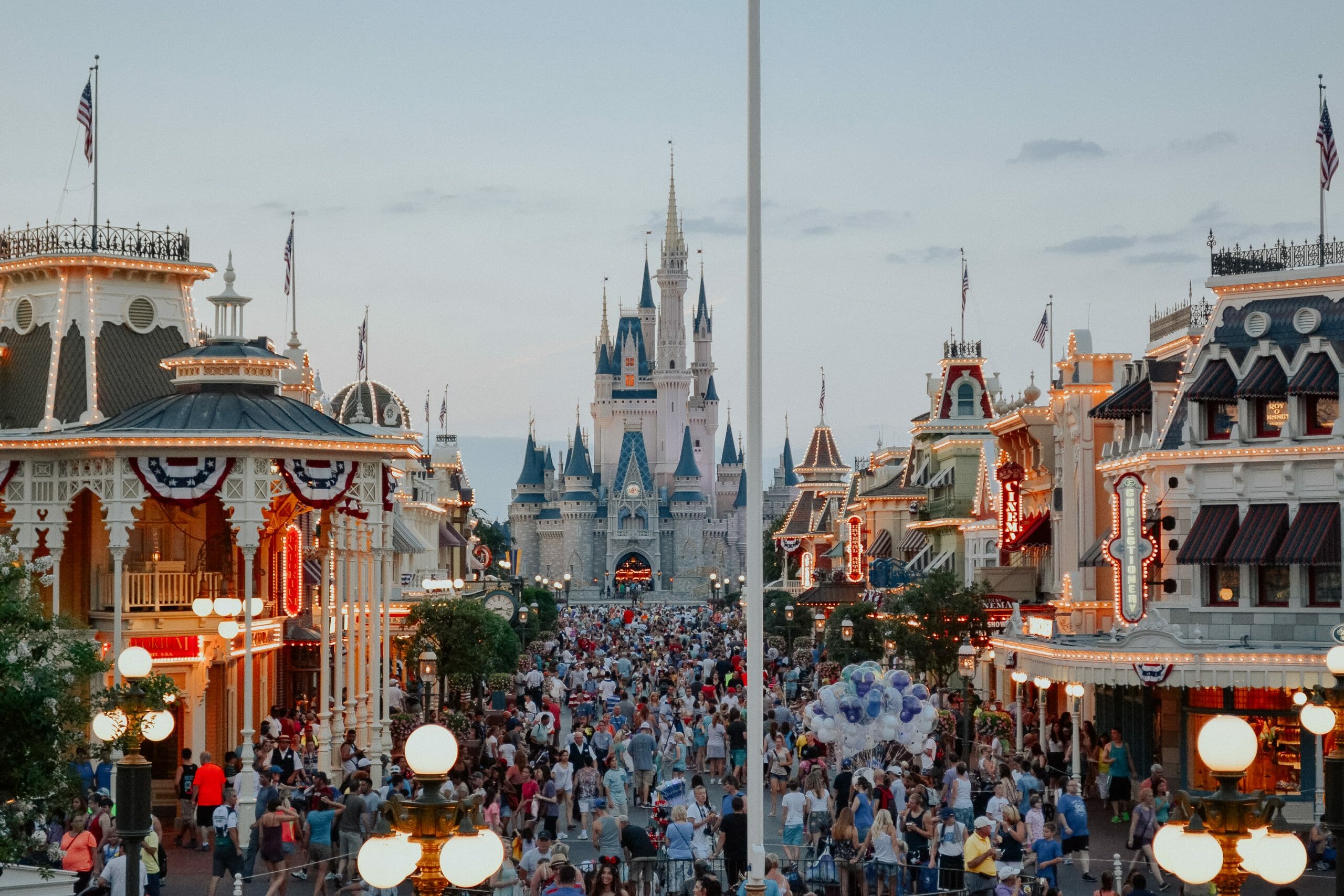 Foto de um dia muito cheio no Magic Kingdom, com o castelo da Cinderela ao fundo e a Main Street começando a ser iluminada.