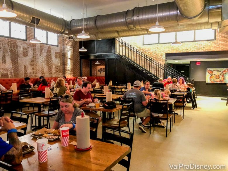 Foto do interior do restaurante The Polite Pig, em Disney Springs, com mesas de madeira e decoração no estilo industrial. 