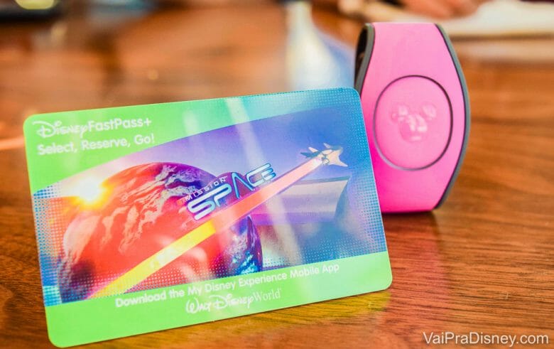 Imagem do cartão magnético que funciona como ingresso da Disney, ao lado de uma MagicBand cor-de-rosa. O cancelamento dos ingressos não é possível, mas é permitida a remarcação. 