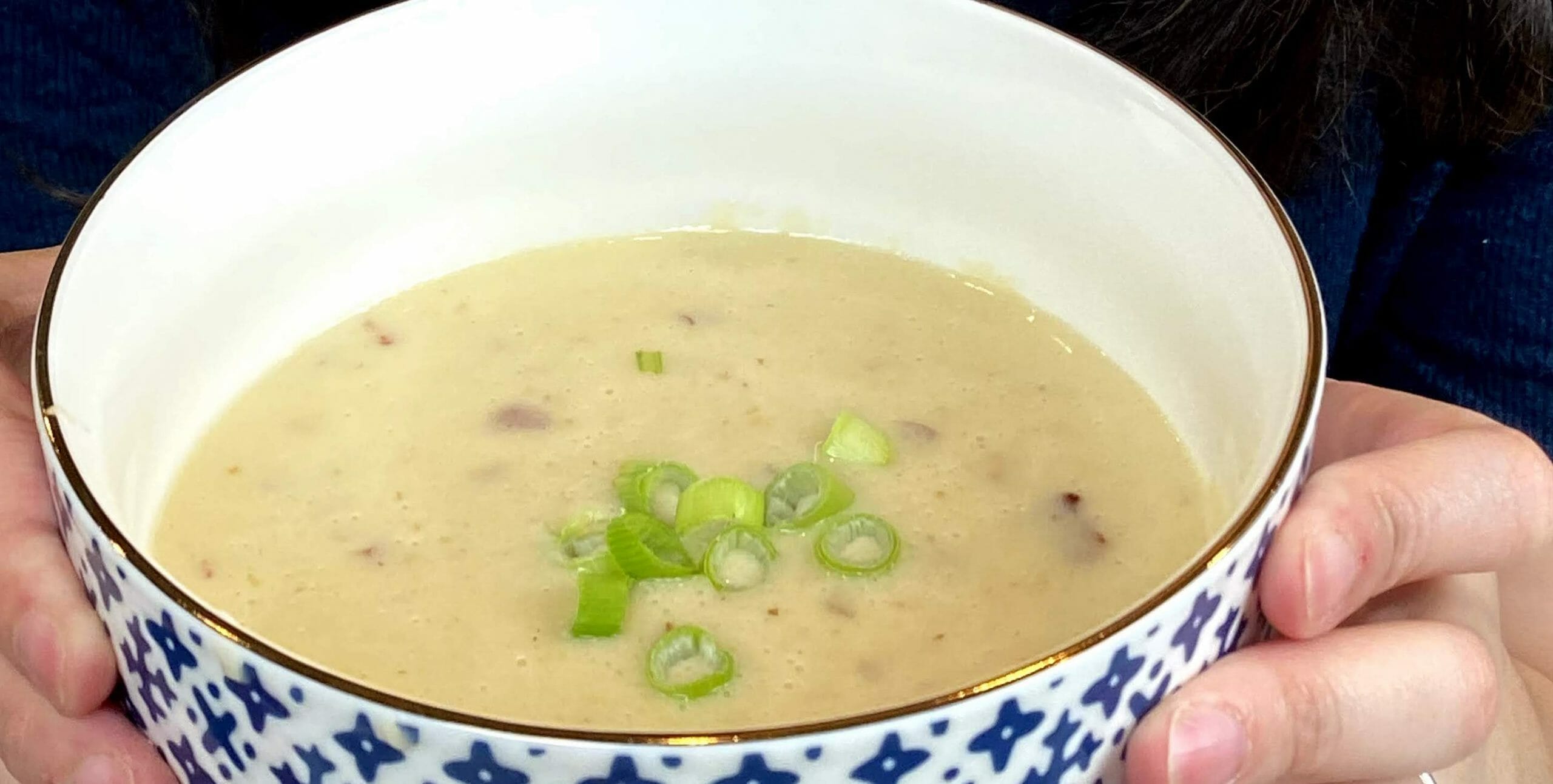 Foto de uma tigela azul e branca com sopa de cheddar, com um pouco de bacon visível e pedaços de cebolinha por cima.