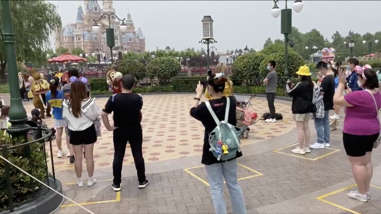 Foto dos visitantes praticando o distanciamento na Disney de Shanghai, respeitando as marcações de quadrados amarelos no chão