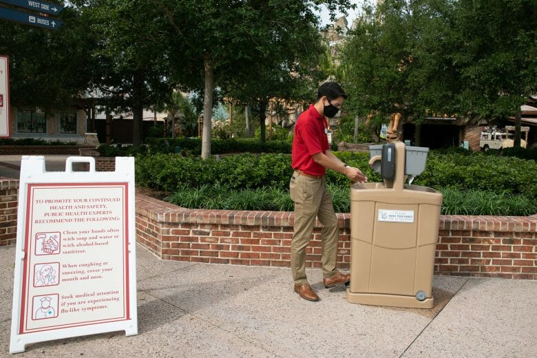 Foto de uma das estações para higienizar as mãos em Disney Springs, com um funcionário de máscara lavando as mãos na pia. 