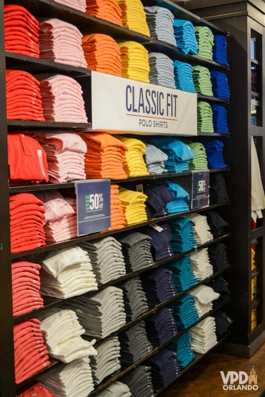 Roupas em Outlet de Orlando: fique atento às medidas! Foto de uma prateleira de camisetas em um outlet, com muitas opções de cores e uma placa indicando "classic fit - polo shirts"